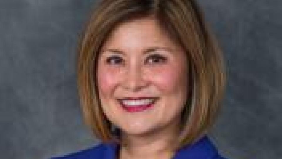 Susan Shin Angulo smiling in blue suit with gray background