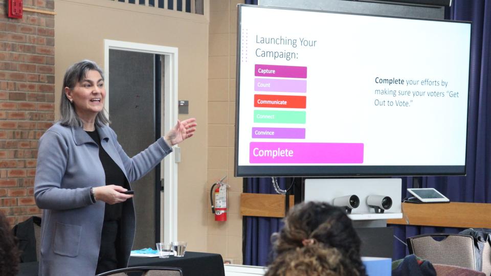 Woman in gray jacket in front of projector screen