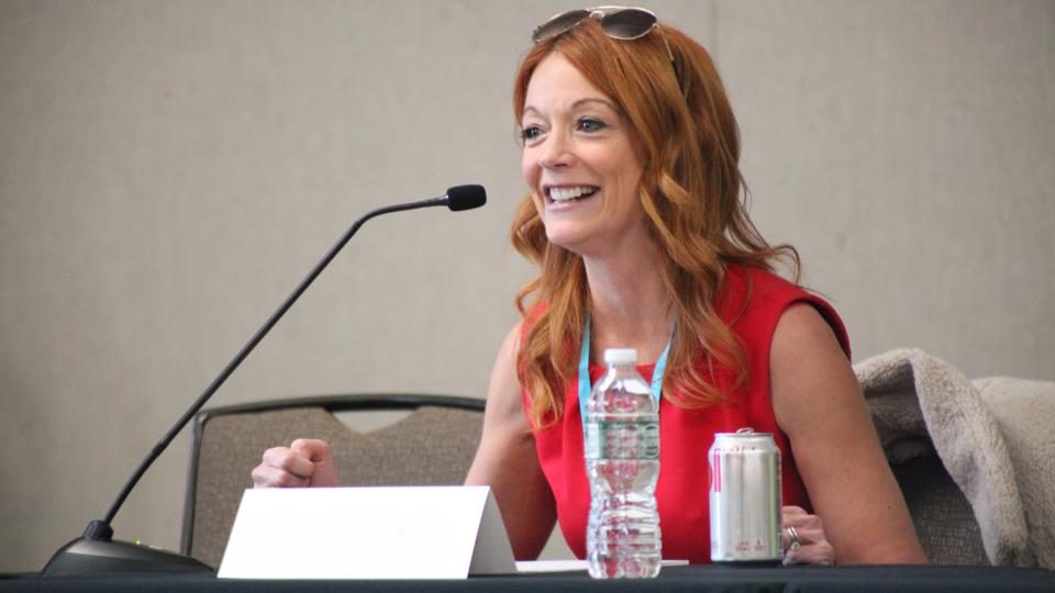 Women in red dress seated at table with a microphone