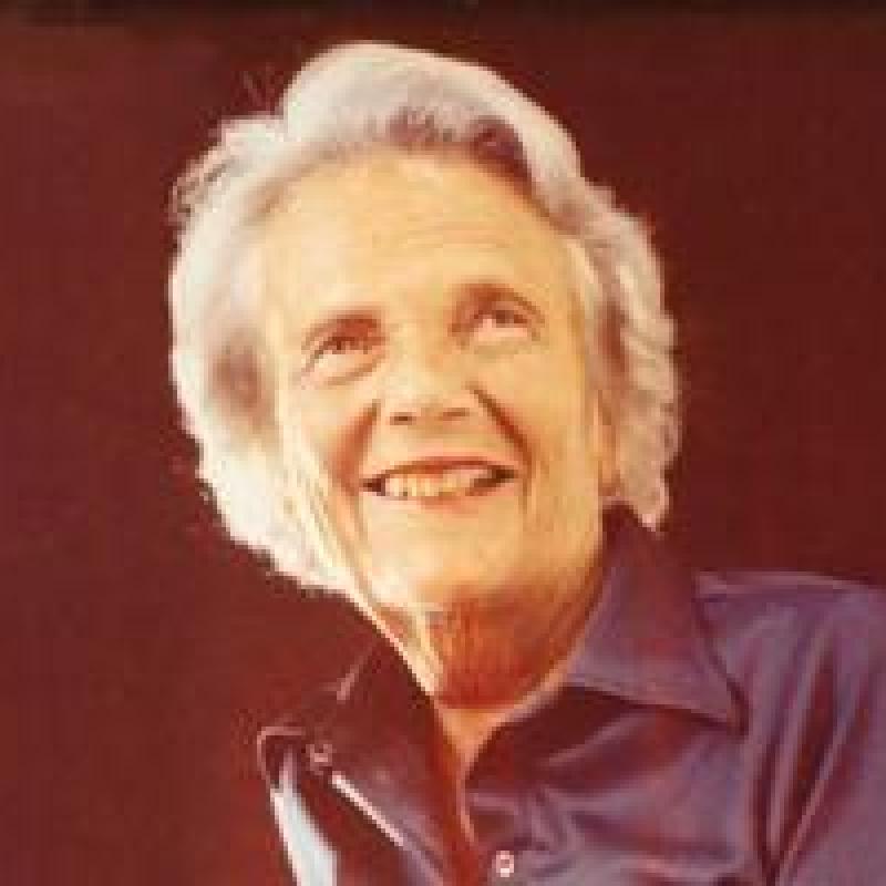 Katherine Neuberger smiling in shiny dark colored blouse with black background 