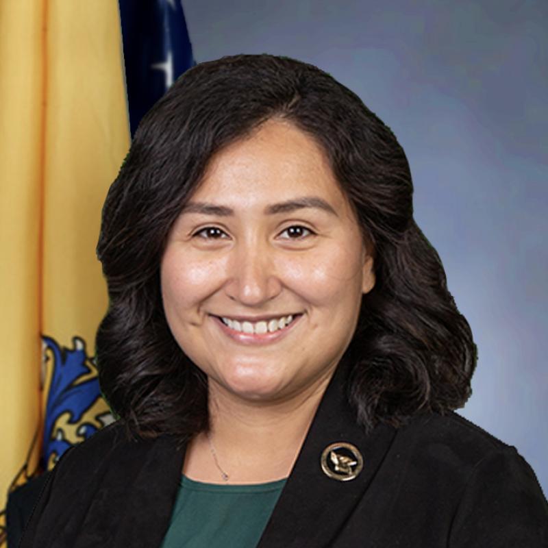Head shot of Josely Castro wearing a black jacket and green shirt against a yellow and blue backdrop 