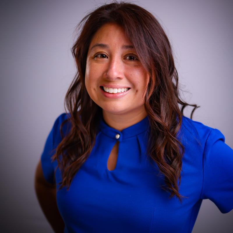 A woman with brown hair wearing a blue shirt smiles at the camera