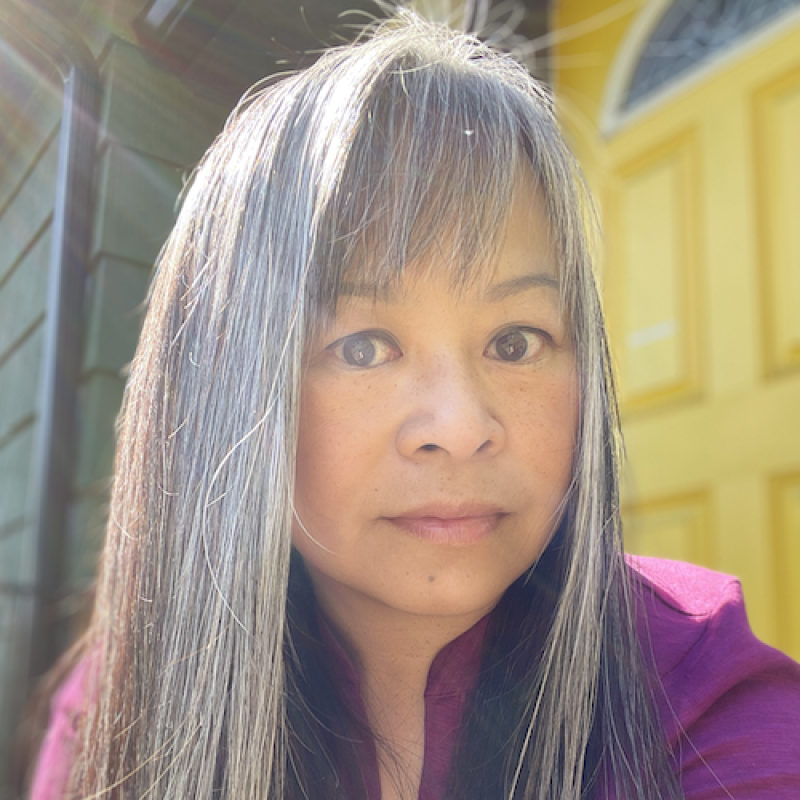 A selfie of a woman with gray hair, sitting outside by a yellow door