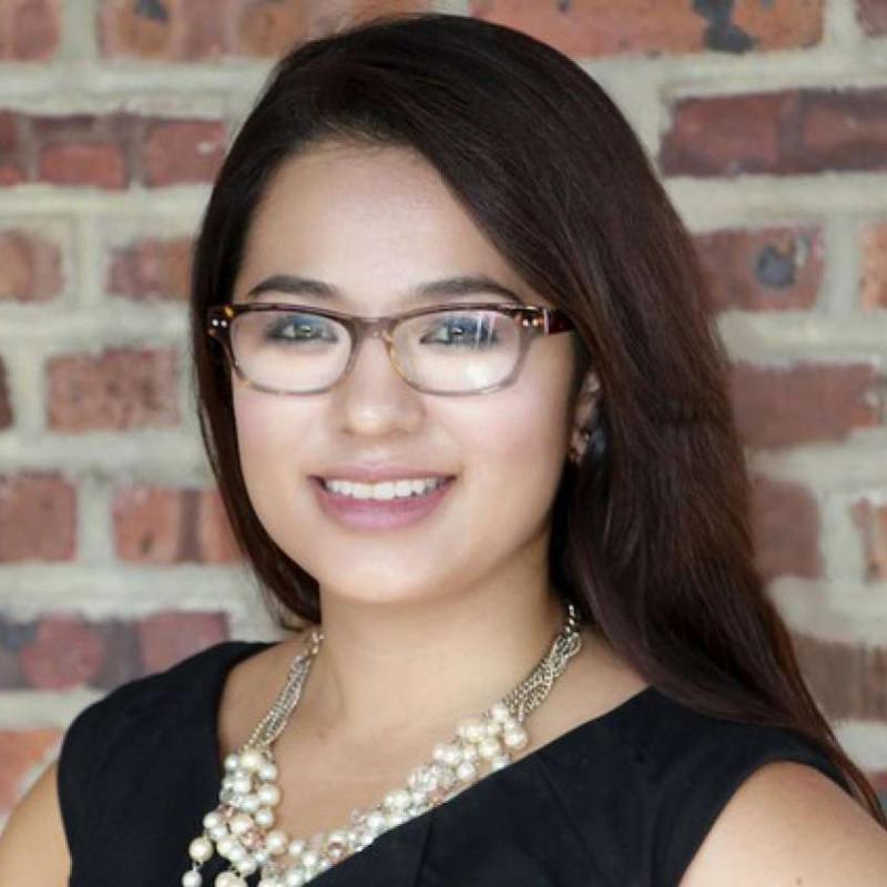 Cristina Pinzon in dark brown glasses posing in front of a brick wall