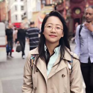 Dan Qi smiling in tan jacket and standing on the street