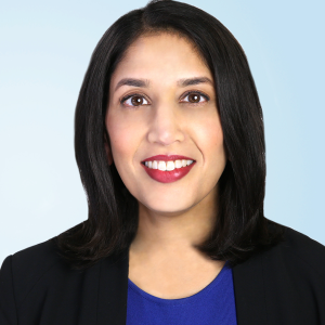 Sameena Mustada in a blue blouse and black blazer in front of a light blue background