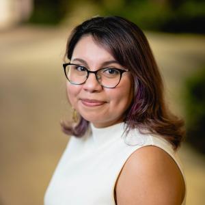 Maricruz Osorio smiling in white blouse in front of blurred background