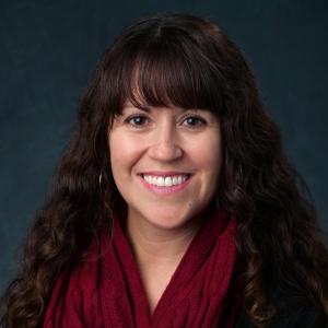 Celeste Montoya with a red scarf in front of a dark background