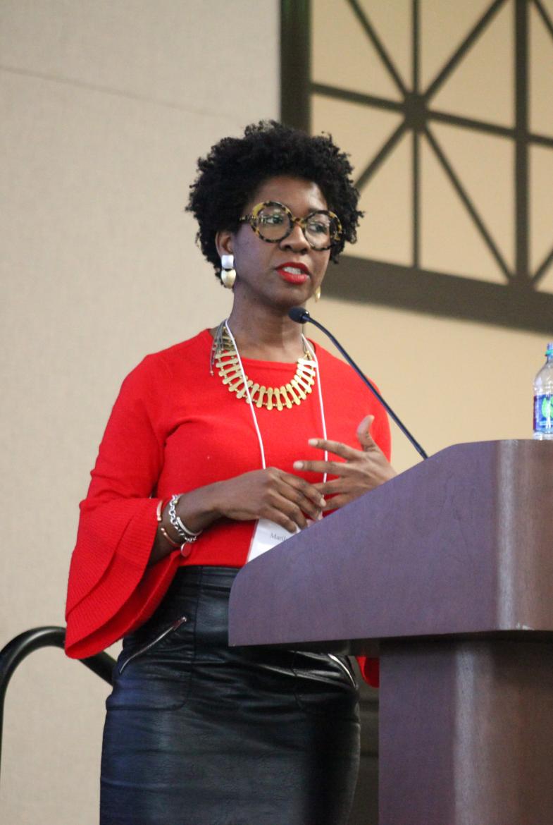 Woman in red blouse and black skirt standing behind wooden podium