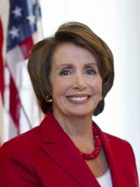 Representative Nancy Pelosi, wearing red suit with American flag behind her